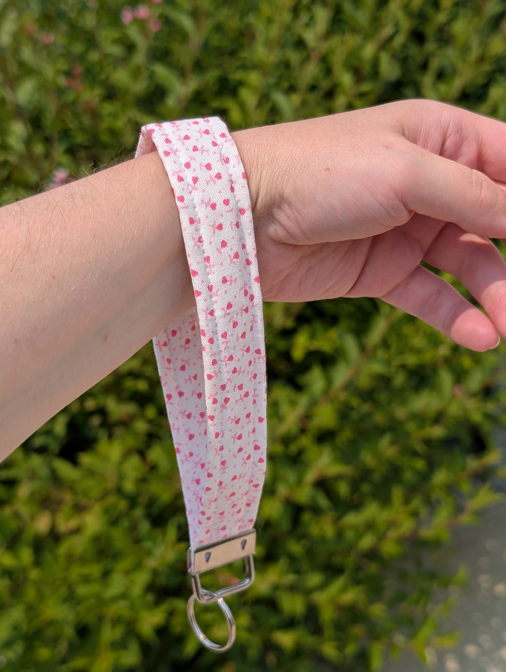 Wristlet with pink floral pattern on wrist against a green outdoor background