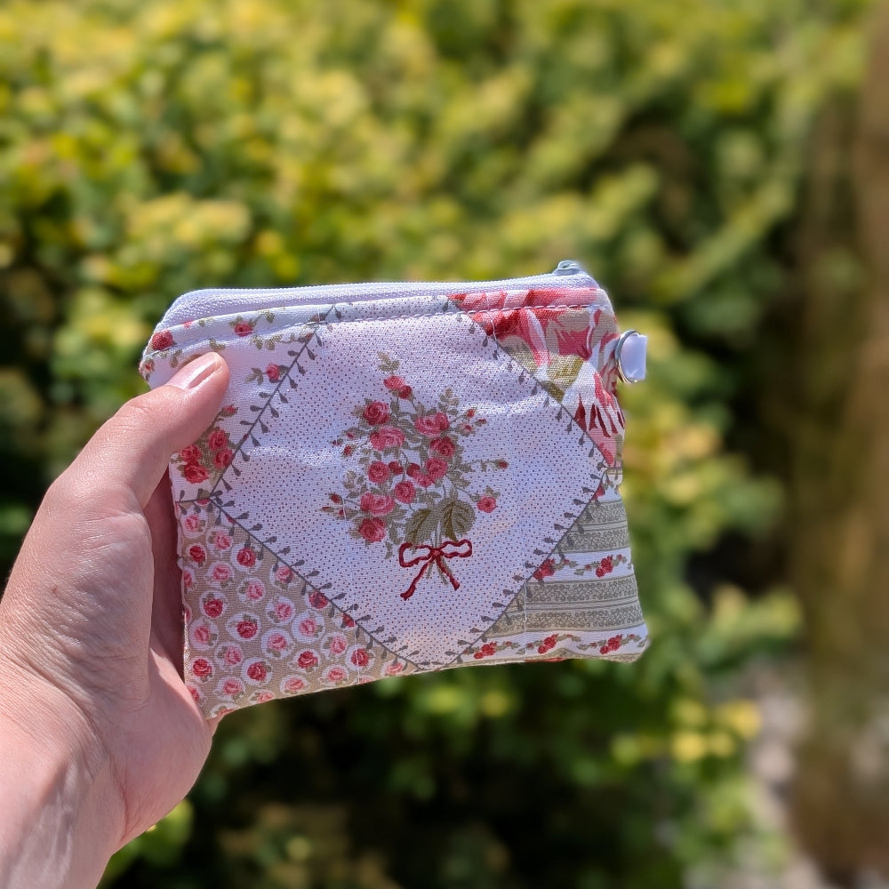 Hand holding a floral-patterned fabric pouch against a blurred green outdoor background