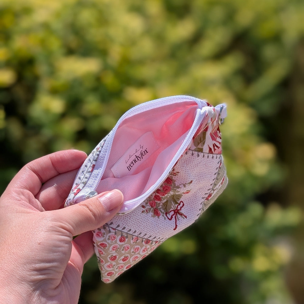 Hand holding a floral-patterned pouch with a pink interior against a blurred green background