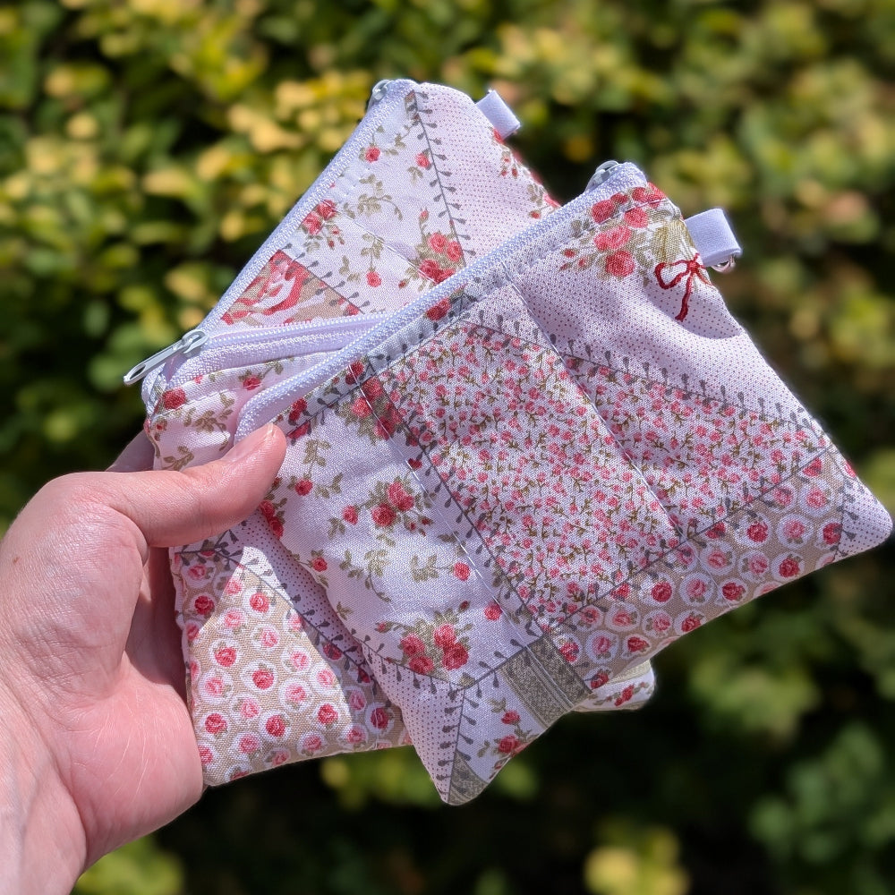 Hand holding three small floral fabric bags against a blurred green outdoor background
