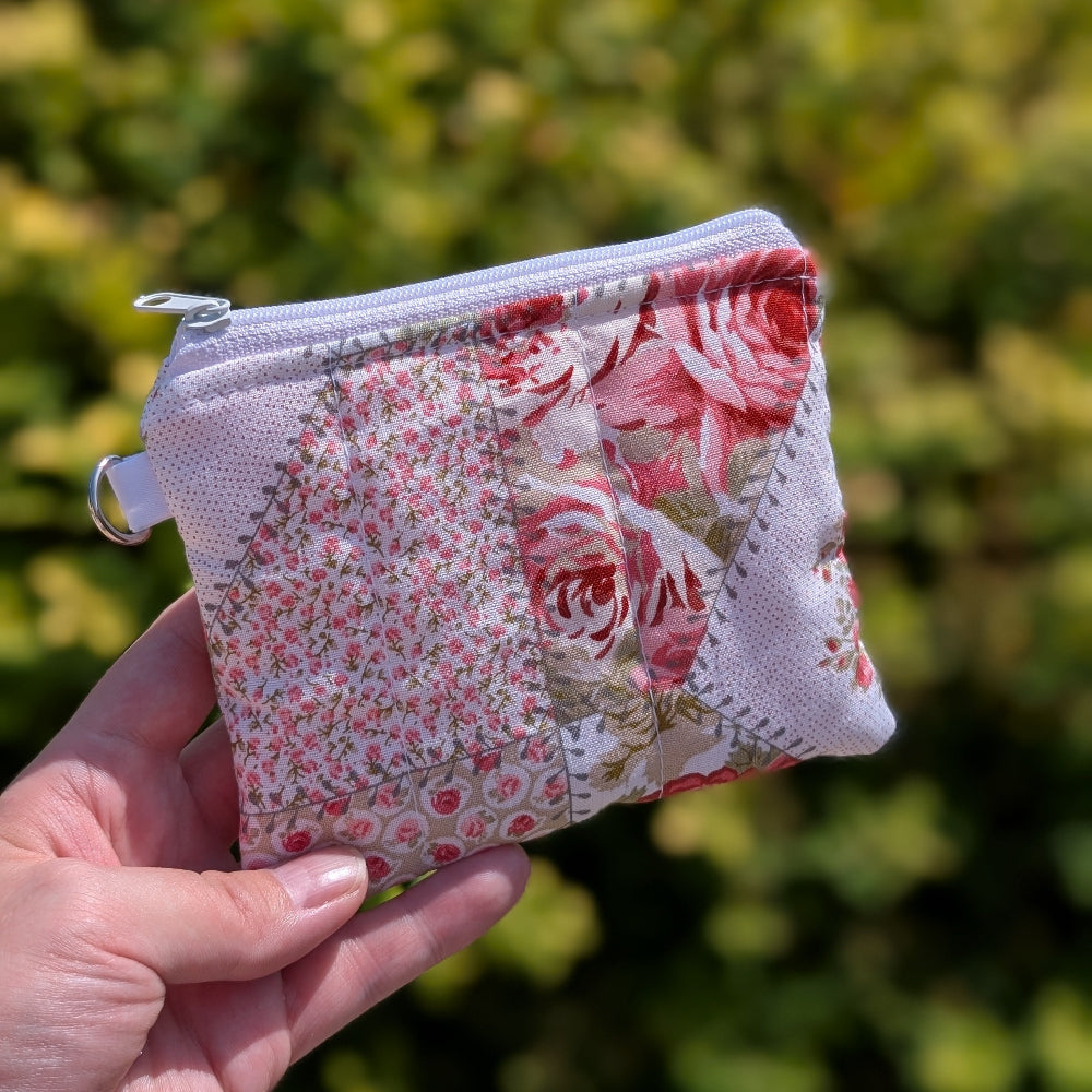Hand holding a small fabric pouch with floral pattern against a blurred green background