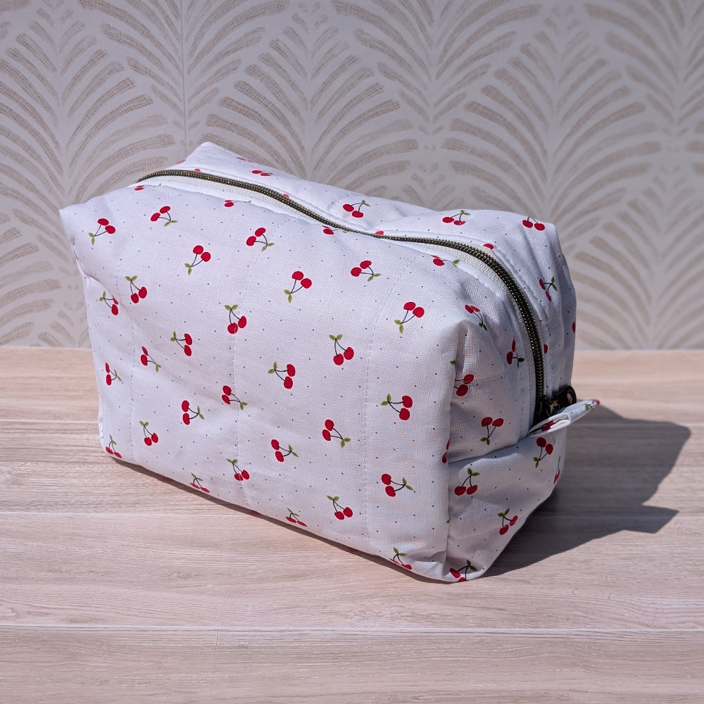 White toiletry bag with red cherry pattern on a wooden surface