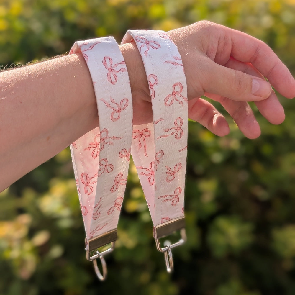 Two pink bow patterned straps on a person's wrist with a blurred green background
