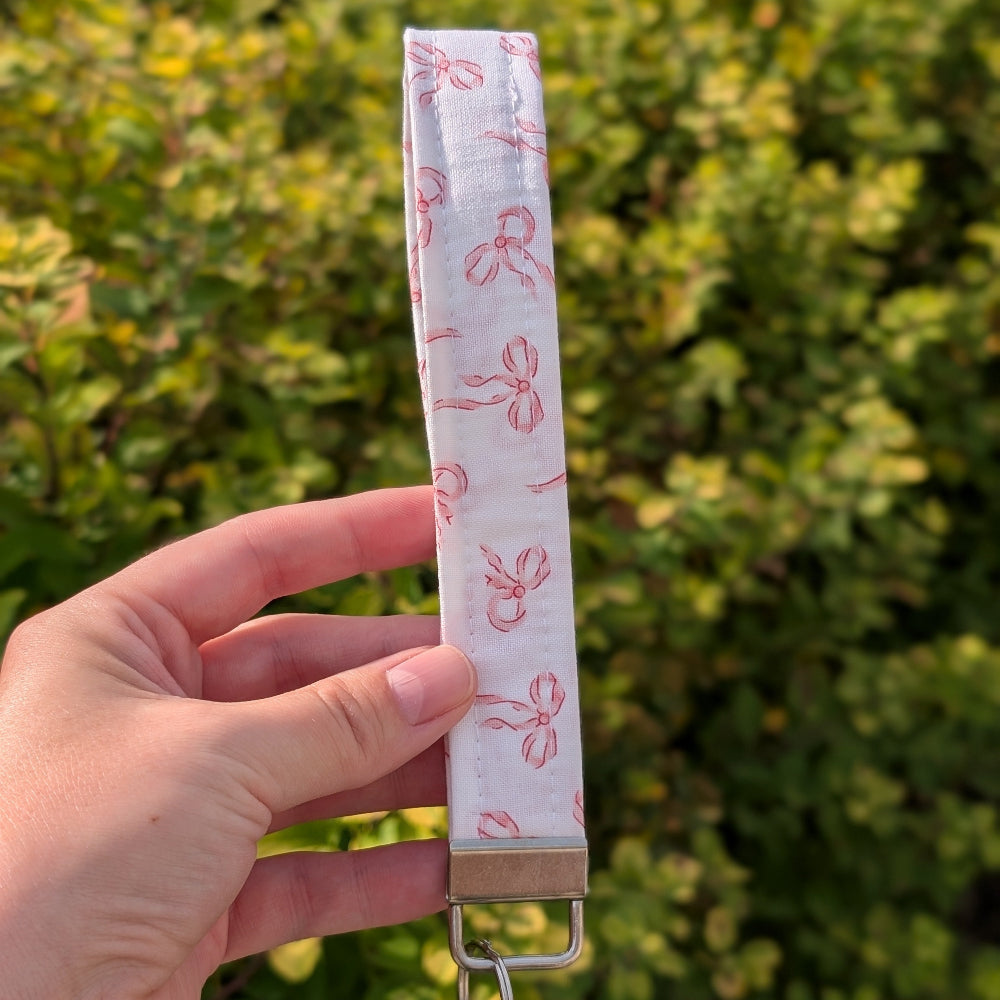 Hand holding a fabric strap with pink floral patterns against a green bush background