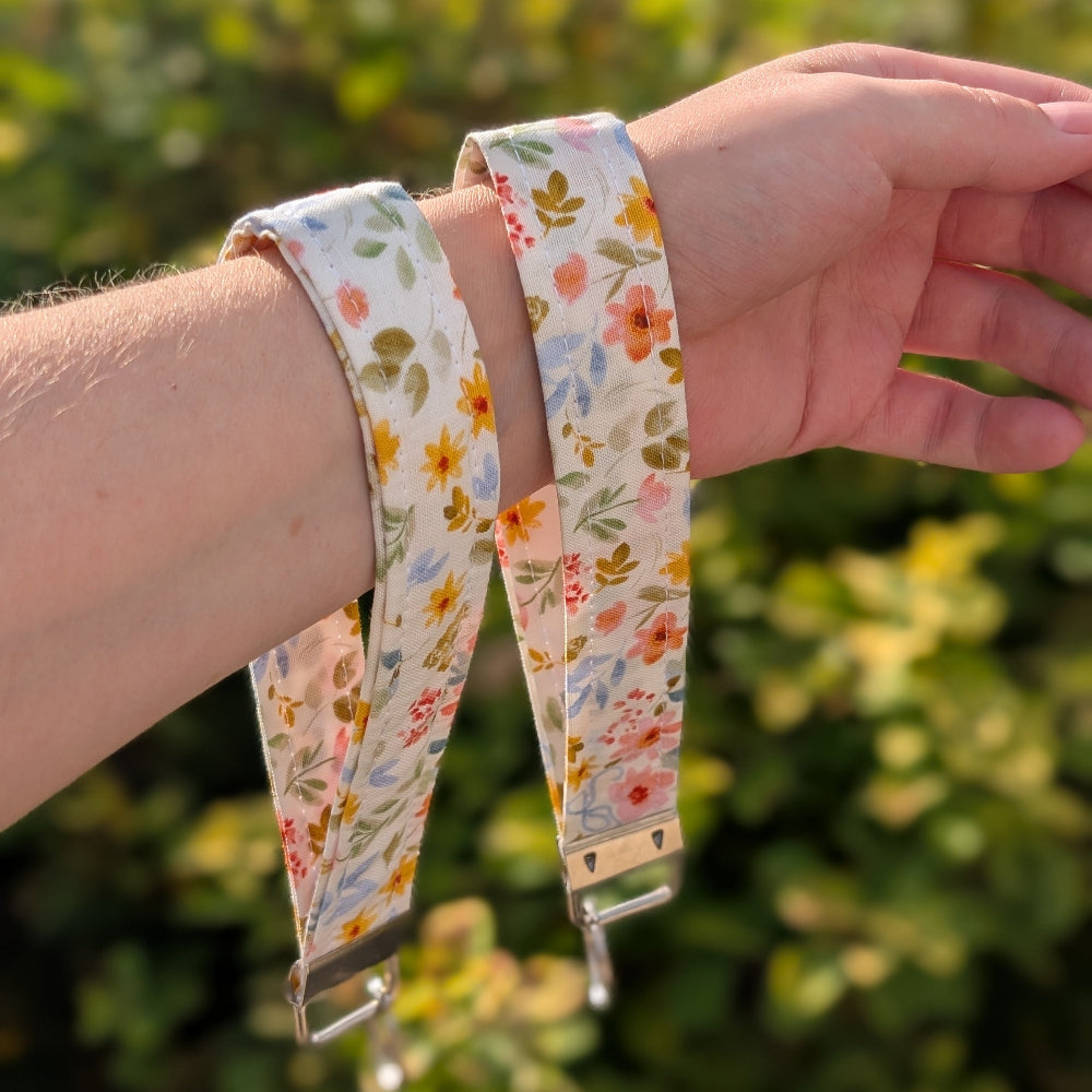 Hand holding two floral-patterned straps against a blurred green background