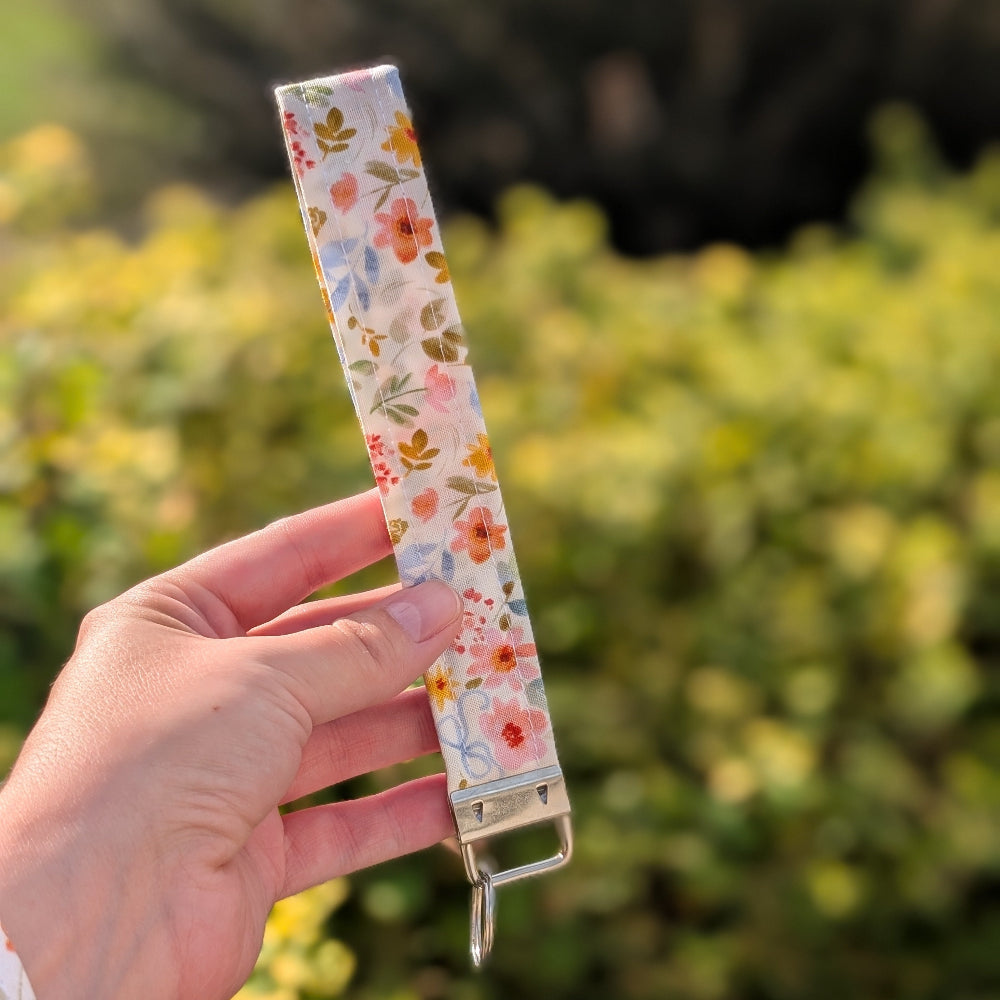 Hand holding a floral-patterned keychain with a blurred green background