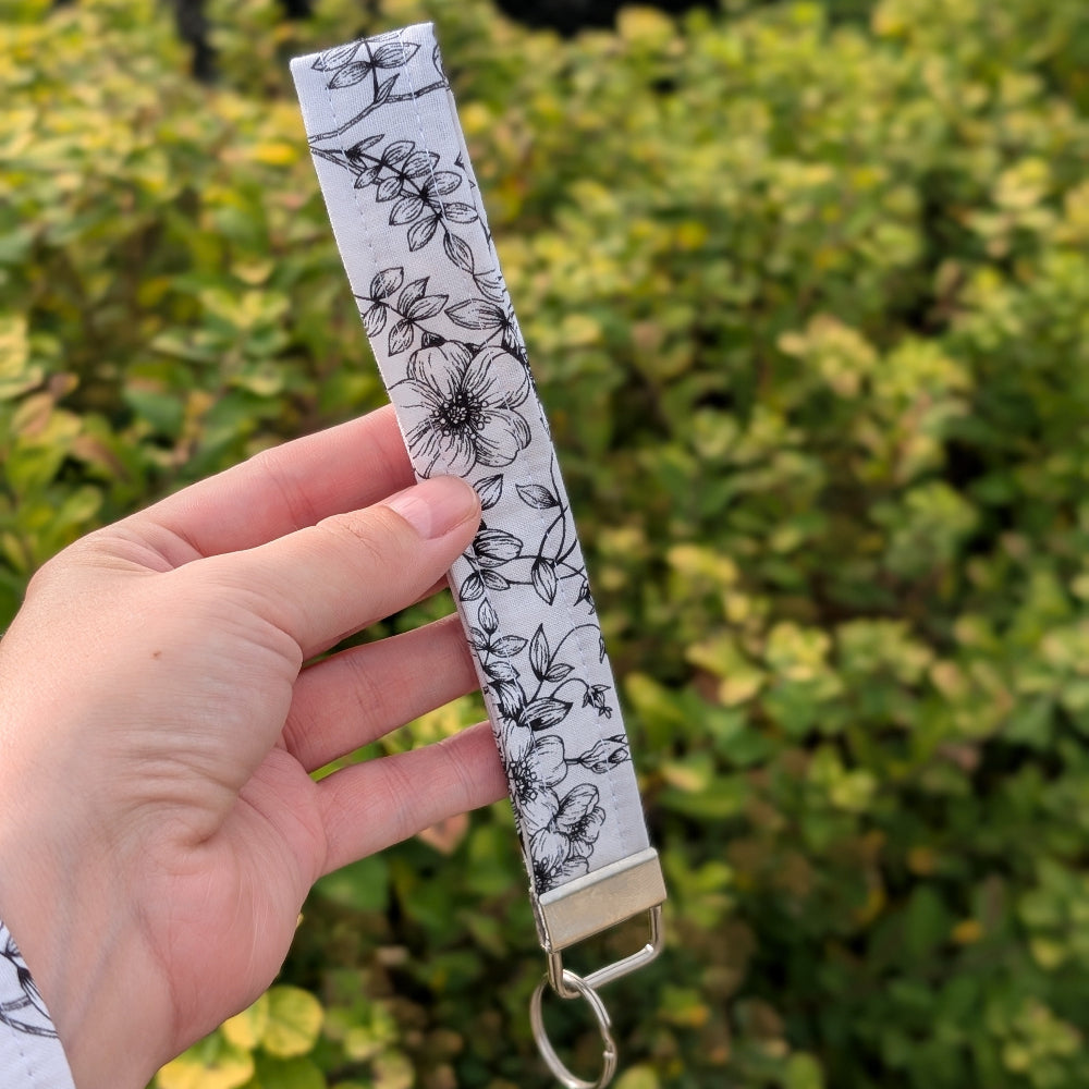 Hand holding a floral-patterned keychain strap against a green bush background