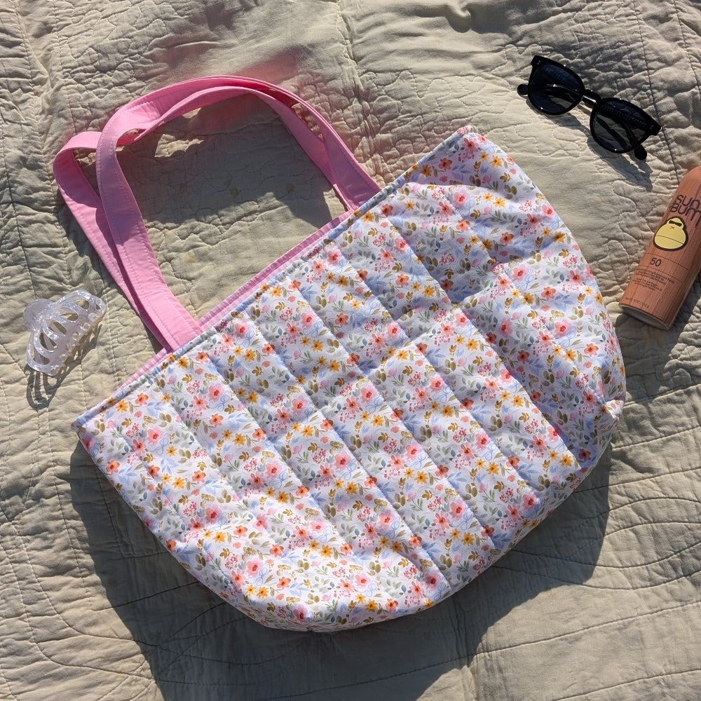 Floral-patterned quilted bag with pink handle on a textured surface