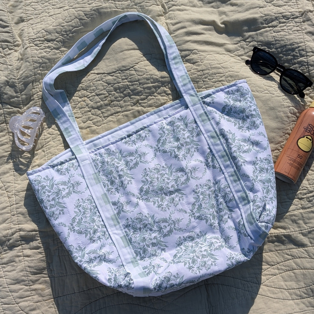 Floral-patterned tote bag on a textured surface with sunglasses and a bottle.