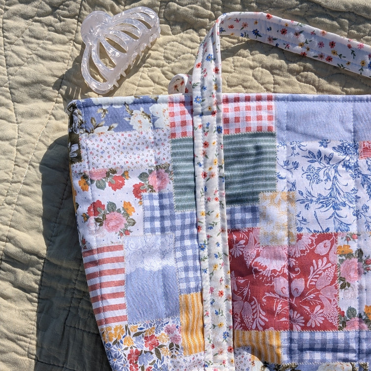Patchwork fabric bag with floral and plaid patterns on a textured surface