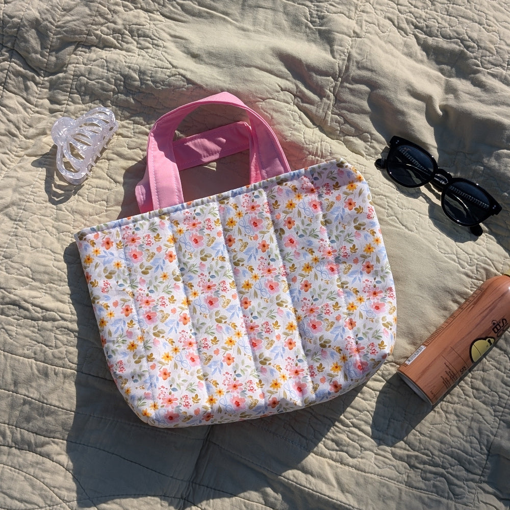 Floral-patterned bag with pink handle on a textured surface