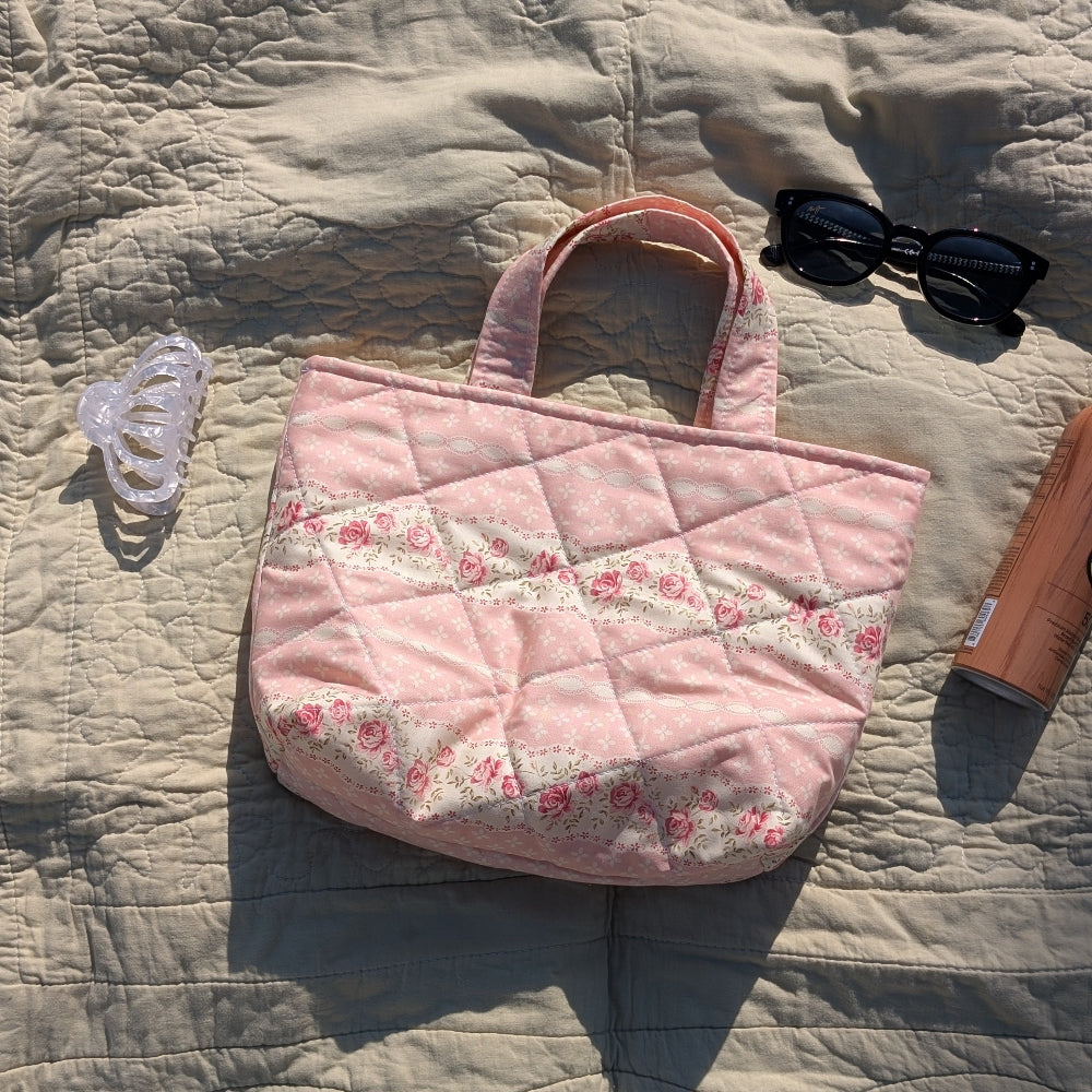 Pink quilted handbag with floral pattern on a textured surface