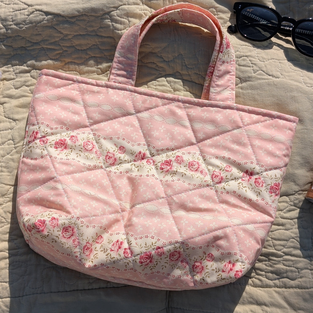 Pink quilted handbag with floral patterns on a beige textured surface