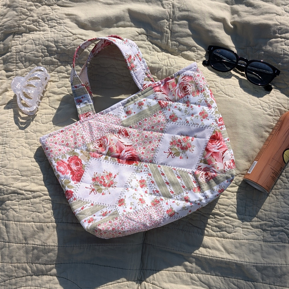 Floral-patterned bag on a textured surface with sunglasses and a bottle.