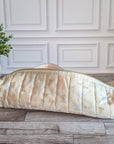 A quilted pencil case with a cream and pale pink floral pattern, resting on a gray wood floor in front of a white paneled wall.